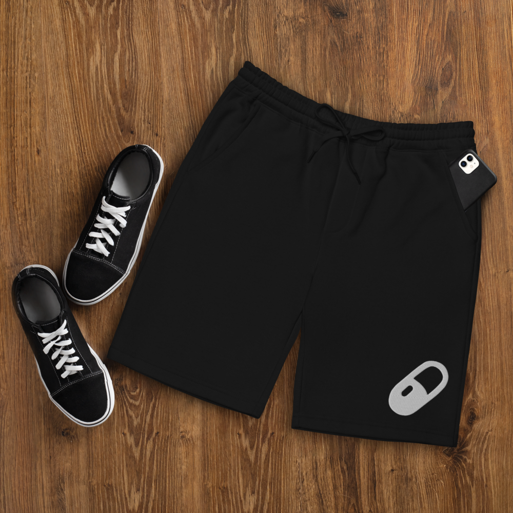 Flat lay of the black fleece shorts styled with black ankle canvas shoes and a phone partially tucked into the right front pocket, suggesting casual functionality.
