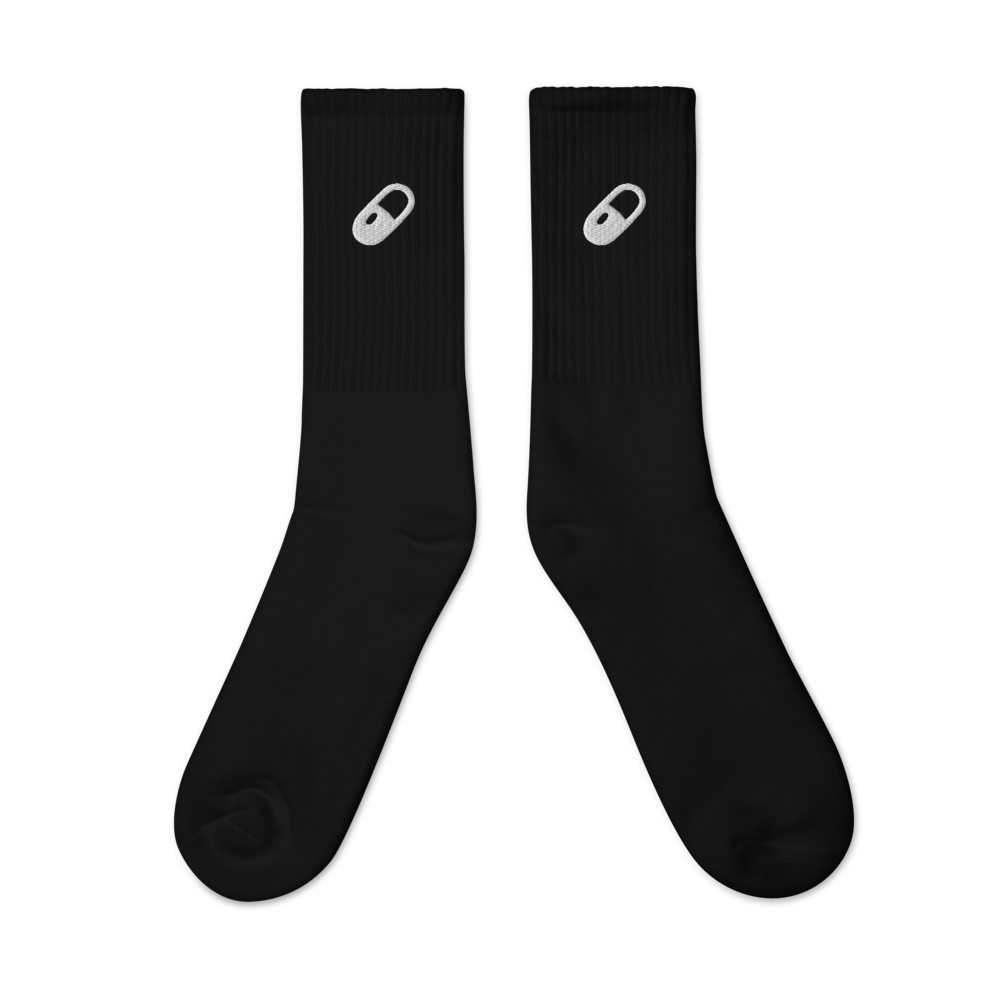 Flat lay of black crew socks featuring a bold white embroidered pill on each side, centered and aligned.