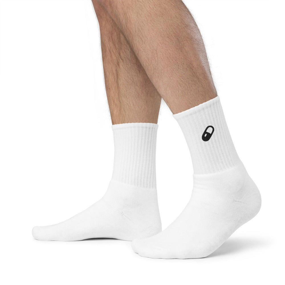 Side view of the model's feet wearing only the white embroidered socks, clearly displaying the pill design and ribbed crew fit.
